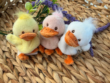 Load image into Gallery viewer, Quack plush bag charms with yellow, blush pink, and white ducks, orange beaks and feet, and silver clasps, displayed on a woven background with purple floral accents.  