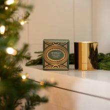 Load image into Gallery viewer, Metallic gold 10 oz. candle and its decorative hunter green and metallic gold box on a white surface with a blurred lit Christmas tree in the foreground.
