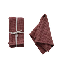 Load image into Gallery viewer, A set of folded red waffle cotton napkins wrapped with a white ribbon, tied in a bow , Next to an identical waffle print napkin, on a white background.  