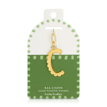 Load image into Gallery viewer, 14K gold-plated hand-painted enamel initial bag charm featuring the letter C with a scalloped edge design and a brushed gold finish, attached to a key ring and clasp. Displayed on a white and green Lucky Feather card with light green dotted brush-stroke borders labeled &quot;Bag Charm Hand Painted Enamel.&quot; Displayed against a white background. 