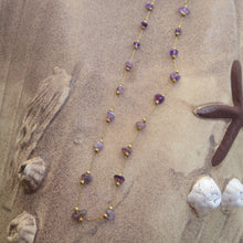 Load image into Gallery viewer, Necklace with purple stones and gold accents on a sandy surface with starfish and shells.
