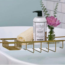 Load image into Gallery viewer, Gold bath caddy with Archipelago Botanicals Coconut body wash in white bottle with black pump, loofah, and a vase with purple flower on a bathtub.