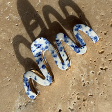 Load image into Gallery viewer, Blue speckle wavy claw clip with gold metal hardware displayed on a beige travertine surface with soft shadows. 