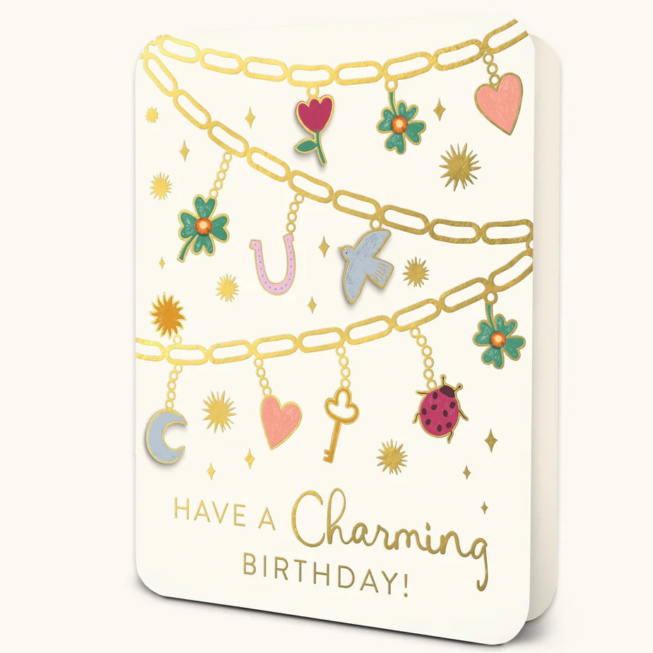 White greeting card featuring gold chain designs with colorful charms including hearts, flowers, a key, moon, horseshoe, bird, and ladybug. Text at the bottom reads 