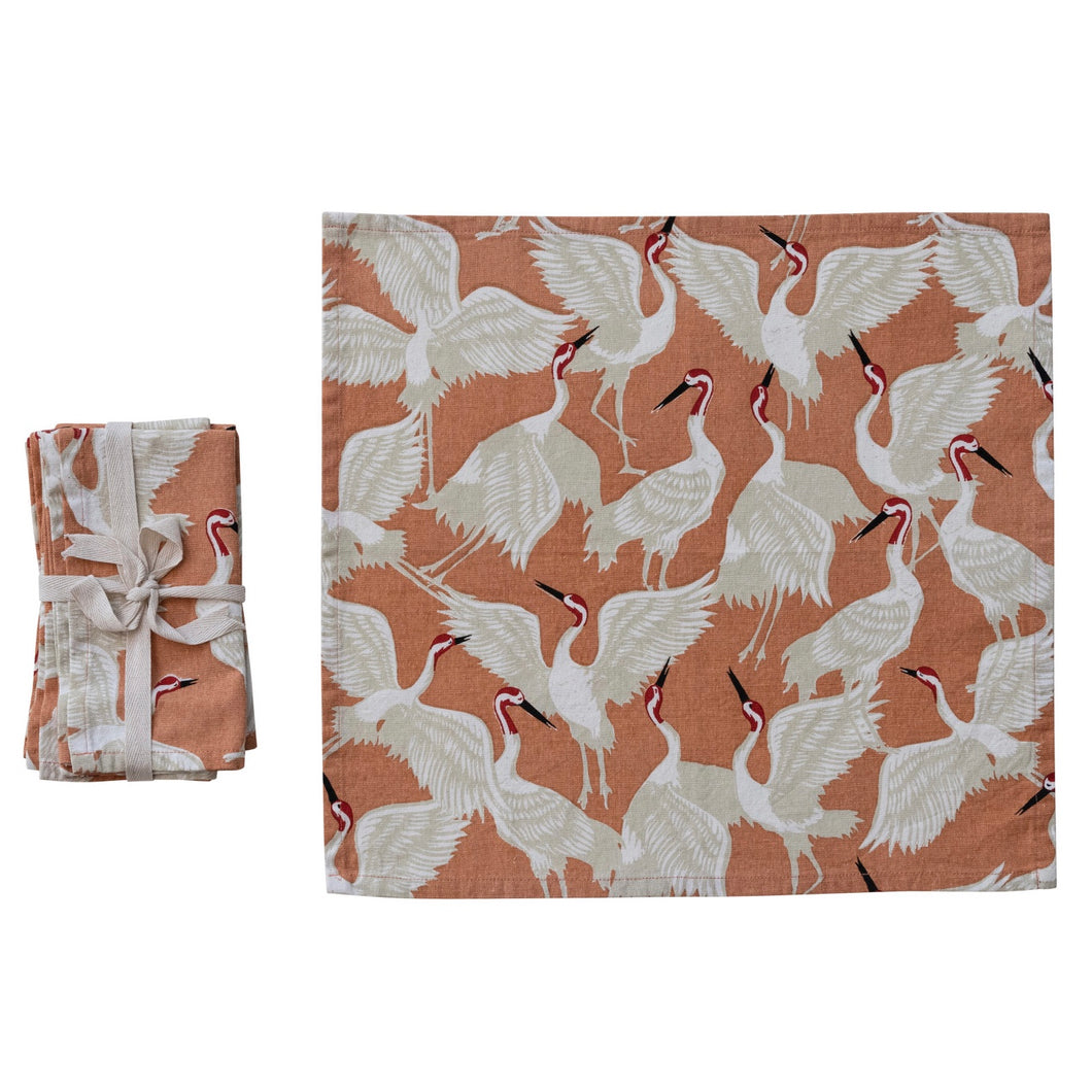 Stack of fabric napkins with a crane bird pattern folded and tied with ribbon, one  unfolded displayed on white background.