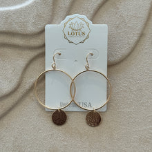 Load image into Gallery viewer, Pair of 14K gold- filled hoop earrings  featuring a hand-hammered round disc charm on each, displayed on a textured tan surface. 