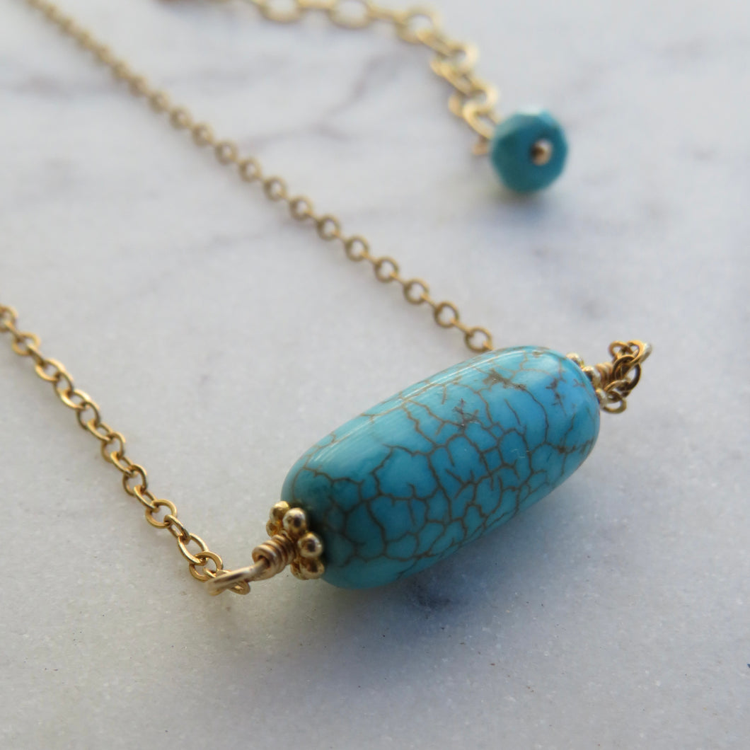 Gold chain necklace with large turquoise bead on a marble surface