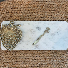 Load image into Gallery viewer, White Marble Cheese Tray, rectangular white marble serving tray with rounded corners and subtle gray veining, a gold-tone textured strawberry-shaped bowl with large veined leaf and curled stem, and a matching spreader with a twisted vine handle and leaf end on a brown woven fiber surface. 