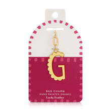 Load image into Gallery viewer, 14K gold-plated hand-painted enamel initial bag charm featuring the letter G with a scalloped edge design and a brushed gold finish, attached to a key ring and clasp. Displayed on a white and deep pink Lucky Feather card with a pink dotted brush-stroke borders labeled &quot;Bag Charm Hand Painted Enamel.&quot; Displayed against a white background.