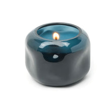 Load image into Gallery viewer, Blue tinted glass candle holder with a lit candle on a white background.