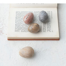 Load image into Gallery viewer, A set of carved marble eggs in pink, blue, beige, and tan colors placed on an open book. On a white textured surface.