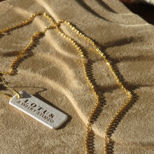 Load image into Gallery viewer, Gold chain necklace displayed on a textured tan surface with a white tag that reads &quot;LOTUS Jewelry Studio&quot; in gold. 