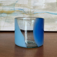 Load image into Gallery viewer, Splash Cup clear hand-blown glass with abstract blue and light blue swirled design on wooden surface against abstract background. 