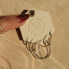 Load image into Gallery viewer, Silver-tone hoop earring set in multiple sizes displayed on a cream LOTUS card held against a textured tan surface. 