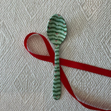 Load image into Gallery viewer, Enameled Holiday Spoons | Four Styles, lifestyle photo of a stainless steel spoon with a mint green enamel background, decorated with green evergreen garlands and small red bows, displayed with a red ribbon on a cream textured fabric surface.  
