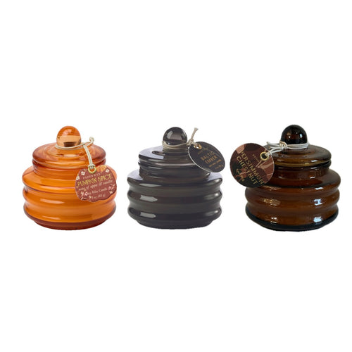 Three glass candles with a ribbed design and knob on top for a handle. Glass candles colors from left to right: pumpkin, dark grey, and dark brown. All against a white background.