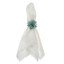 Load image into Gallery viewer, White cloth napkin secured with a sea-blue beaded napkin ring featuring a floral motif, displayed on a white background. 