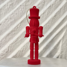 Load image into Gallery viewer, Red nutcracker ornament holding a small drum and drumsticks, standing upright with a gold hanging cord against a white background. 