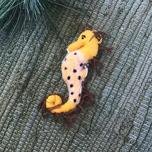 Felt yellow seahorse plush on a green quilted background. 