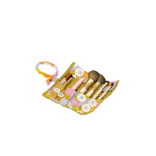 Load image into Gallery viewer, Floral makeup brush roll with a mustard yellow interior and a pink, orange, lavender, and white retro flower pattern, shown open and filled with assorted makeup brushed and tools, displayed on a black and gray checkered background.  