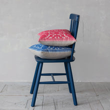 Load image into Gallery viewer, Two patterned cushions, one blue and one red, on a blue chair against a gray wall.