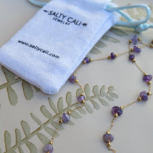Load image into Gallery viewer, Necklace with purple stones and gold accents on a beige surface with &#39;Salty Cali Jewelry&#39; drawstring pouch.