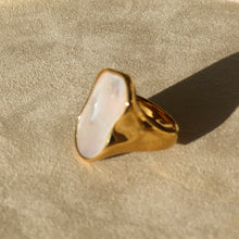 Load image into Gallery viewer, Gold-plated ring with an organic-shaped Mother-of-Pearl face, positioned at a slight angel on a soft textured tan surface with a warm shadow.
