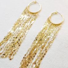 Load image into Gallery viewer, Pair of IP gold-plated brass hoop earrings with long cascading faceted gold chain strands, displayed on a soft white textured background. 
