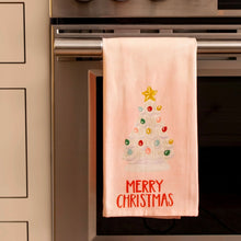 Load image into Gallery viewer, Cotton kitchen towel with a vintage-style white Christmas tree and red &quot;Merry Christmas&quot; text draped over a stainless steel oven handle in a modern kitchen. 