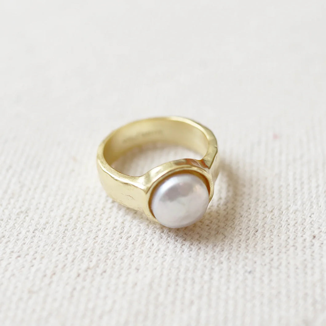 14K gold semi-matte double plated brass casting ring with a freshwater white pearl in a bezel setting. Ring is resting on a cream woven fabric surface. 