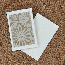 Load image into Gallery viewer, Colby Cards, lifestyle image of a white Lokta paper greeting card featuring an oversized cream and taupe floral print within a white border, displayed with a white envelope on a brown woven mat.