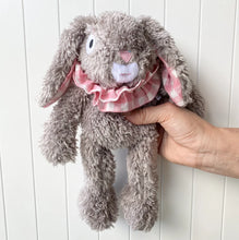Load image into Gallery viewer, Silver gray plush bunny with floppy ears lined in pink and white gingham and a matching ruffled collar, shown being held upright in front of a white paneled background. 