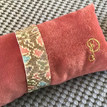 Load image into Gallery viewer, A beaded band bracelet with pink, blue, and brown leopard spots on a pink cushion with a &quot;P&quot; embroidery. On a gray textured surface.