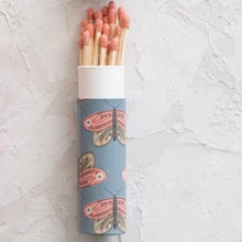 Load image into Gallery viewer, An opened tube of matchsticks. Tube is blue with a butterfly pattern. Red tipped matches inside tube. Laying on a white textured surface.