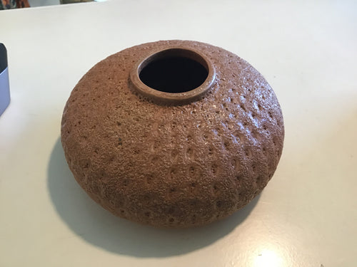 A brown ceramic pot with a textured surface on a white surface.