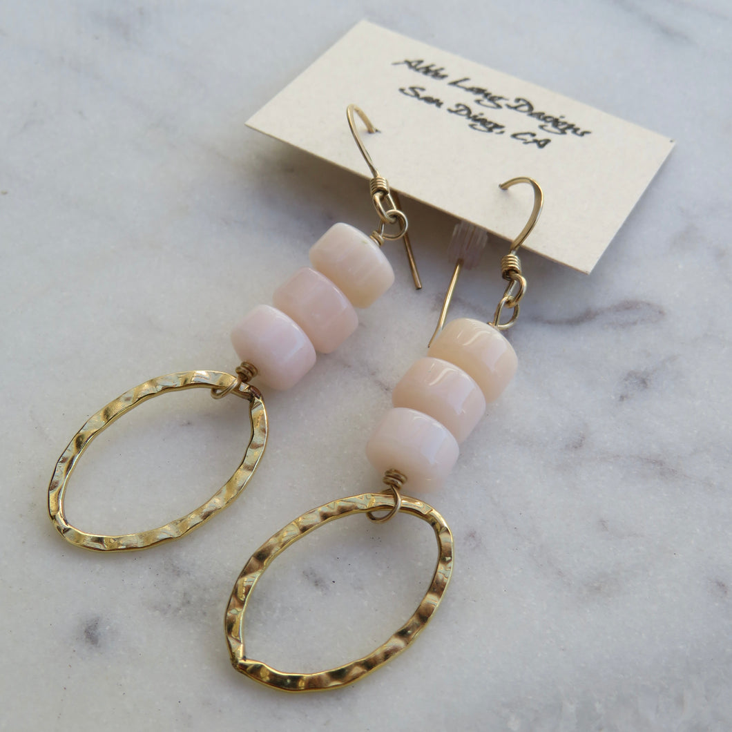 Pair of earrings with 3 stacked  pink beads and gold loops on a marble surface with a 
