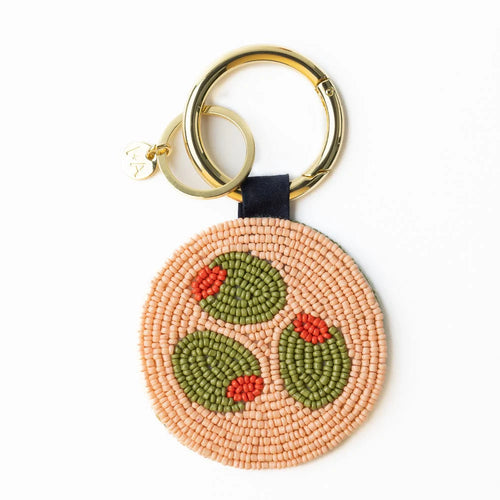 Keychain with a gold circular clip. Keychain is circular made up of peach colored beads and green beads in the shape of olives. On a white background.