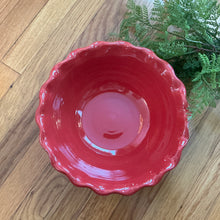 Load image into Gallery viewer, Red stoneware bowl with a scalloped rim viewed from above on a wooden surface with greenery on the upper right side. 