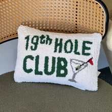 Load image into Gallery viewer, White hooked accent pillow with green "19th Hole Club" text and a martini glass with a red flagstick, displayed on a cane chair. 