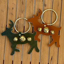Load image into Gallery viewer, A hunter green deer shaped metal ornament with three gold jingle bells and a silver metal ring ; next to a brown deer shaped metal ornament with three gold jingle bells and a silver metal ring. Ornaments lying flat on a brown wooden slat surface.  
