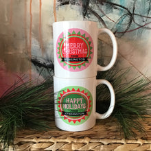 Load image into Gallery viewer, Two white mugs stacked on top of each other. One has a mainly pink and read print that reads &quot;Merry Christmas from Kensington&quot; and the other is mainly green that reads &quot;Happy Holidays from Kensington&quot;. Background is an abstract painting and faux pine needles