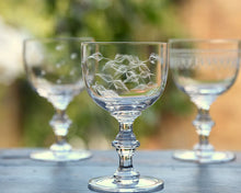 Load image into Gallery viewer, Stemmed goblet with etched leaves. Two more goblets are blurred in the background. All sitting on a wooden platform. Blurred nature background. 