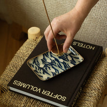 Load image into Gallery viewer, Hand placing an incense holder on a blue-and-white patterned enameled tray with painted gold edging, resting on a book.