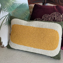 Load image into Gallery viewer, Beaded Lumbar Pillow, mustard yellow, white, and olive green lumbar pillow with geometric beaded pattern, displayed on a light-colored fabric surface with palm frond hardcover book and maroon snake lumbar pillow in background.