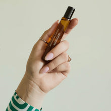 Load image into Gallery viewer, Hand holding amber glass Botanico de Havana personal fragrance rollerball with black cap against a white background.