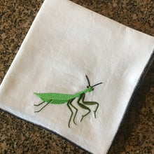 Load image into Gallery viewer, White tea towel with a green embroidered praying mantis on a brown marble surface