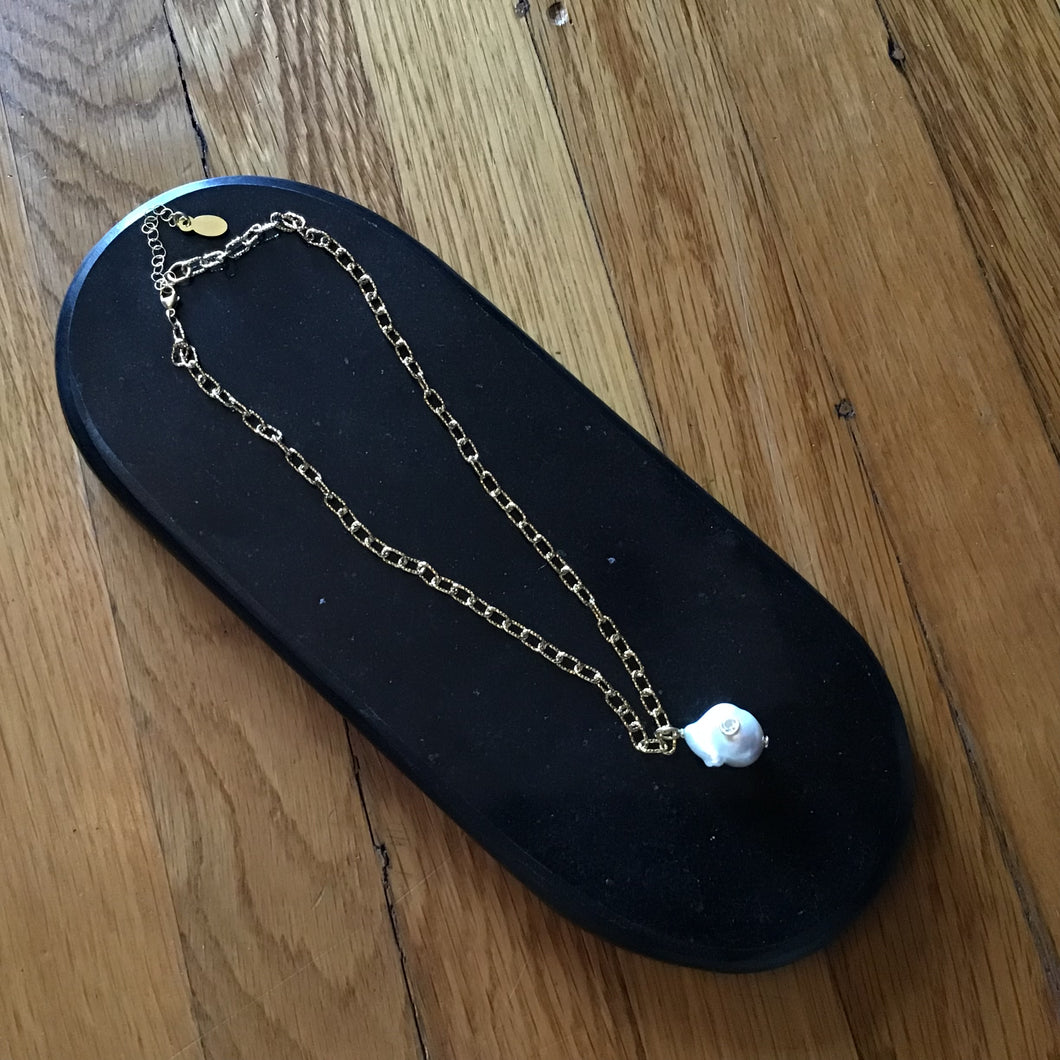 A large pearl necklace with a gold chain displayed on a black surface, on a wooden surface .