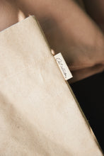 Load image into Gallery viewer, Close-up detail of natural cotton canvas fabric with stitched side seam and brand tag.