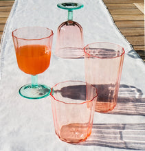 Load image into Gallery viewer, Two clear pink scallop glass goblets with  scalloped rims and green bases, displayed with matching clear pink glassware on a white cloth over a wooden surface. 