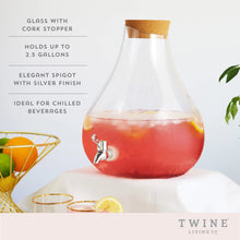 Load image into Gallery viewer, Clear glass beverage dispenser with a silver-colored spigot and a cork stopper, filled with a red drink and citrus slices, shown in a product feature graphic  
